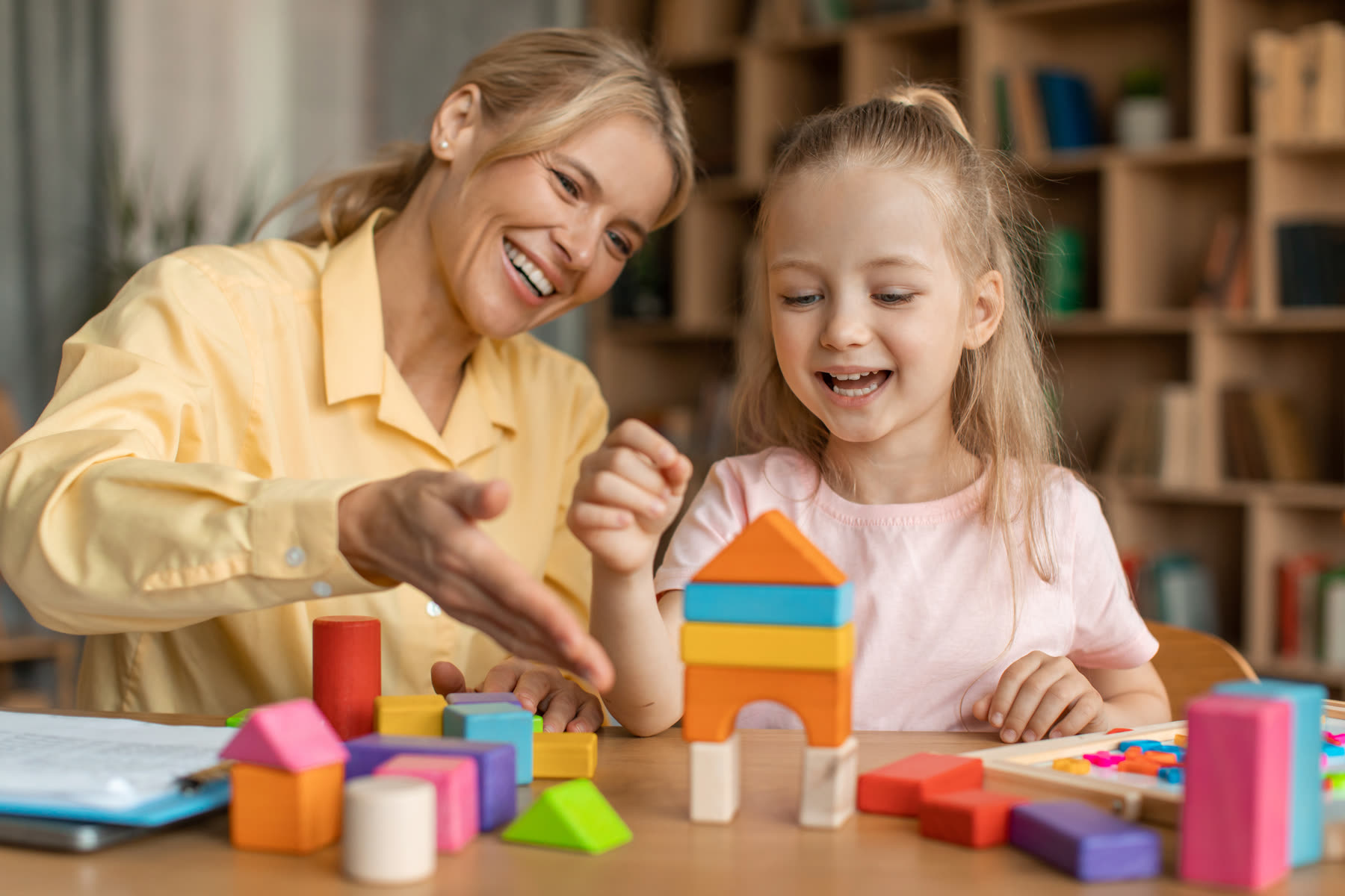 A smiling specialist building with colorful blocks alongside a little girl