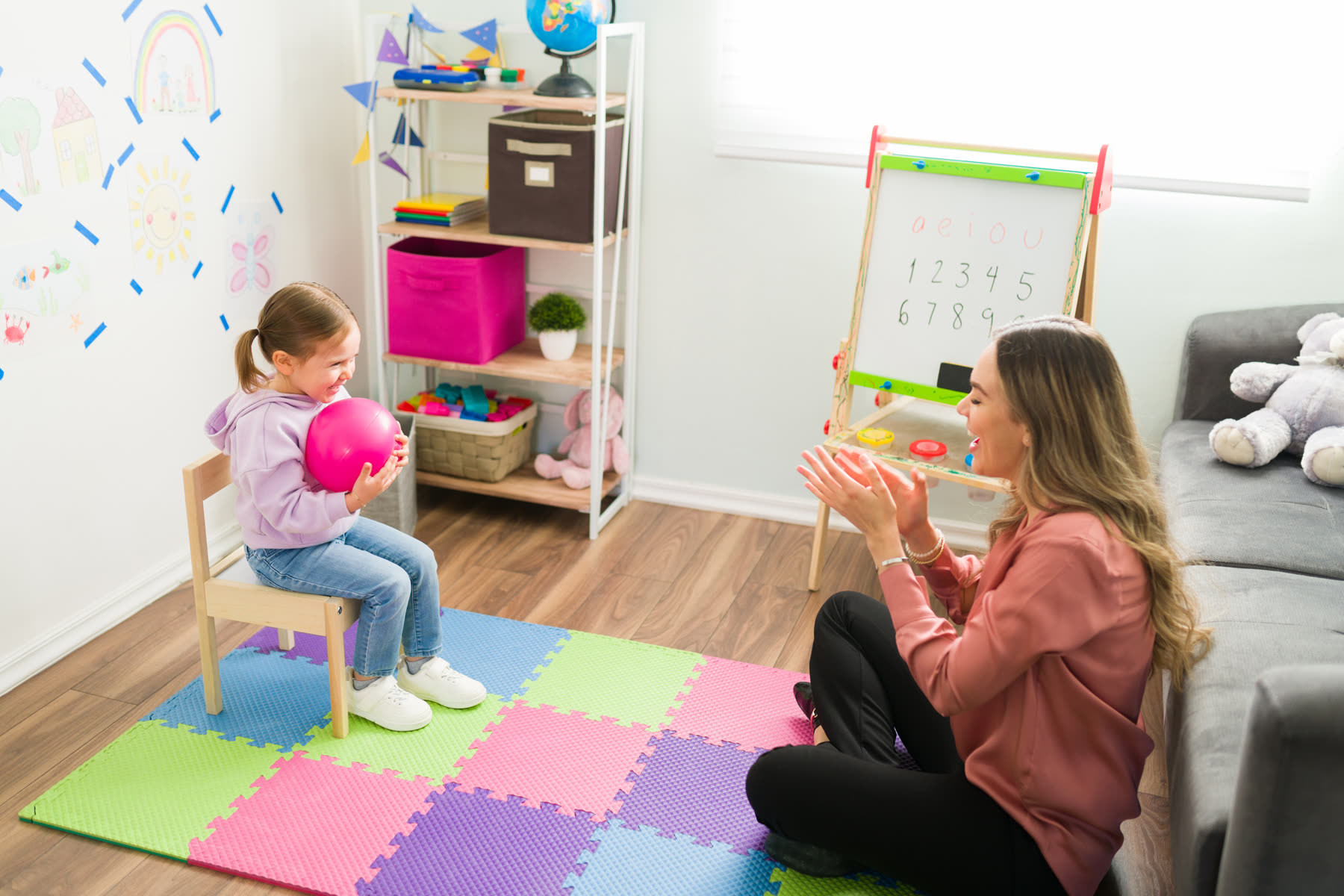 A therapist cheering on a young girl in a bright playroom