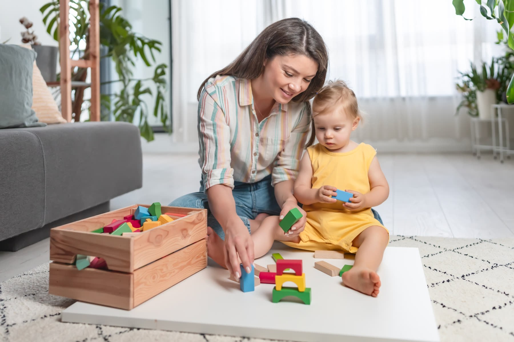 A mother playing with blocks alongside her toddler daughter at home