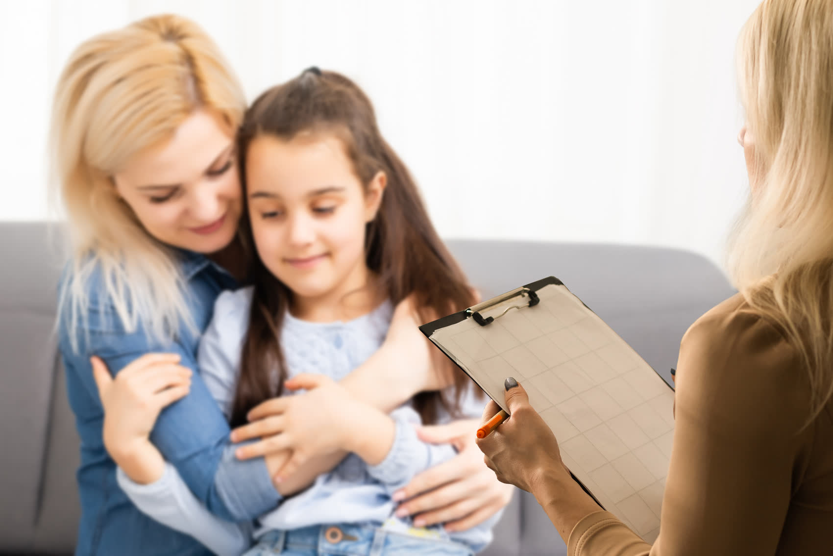A mother hugging her daughter while a counselor takes notes