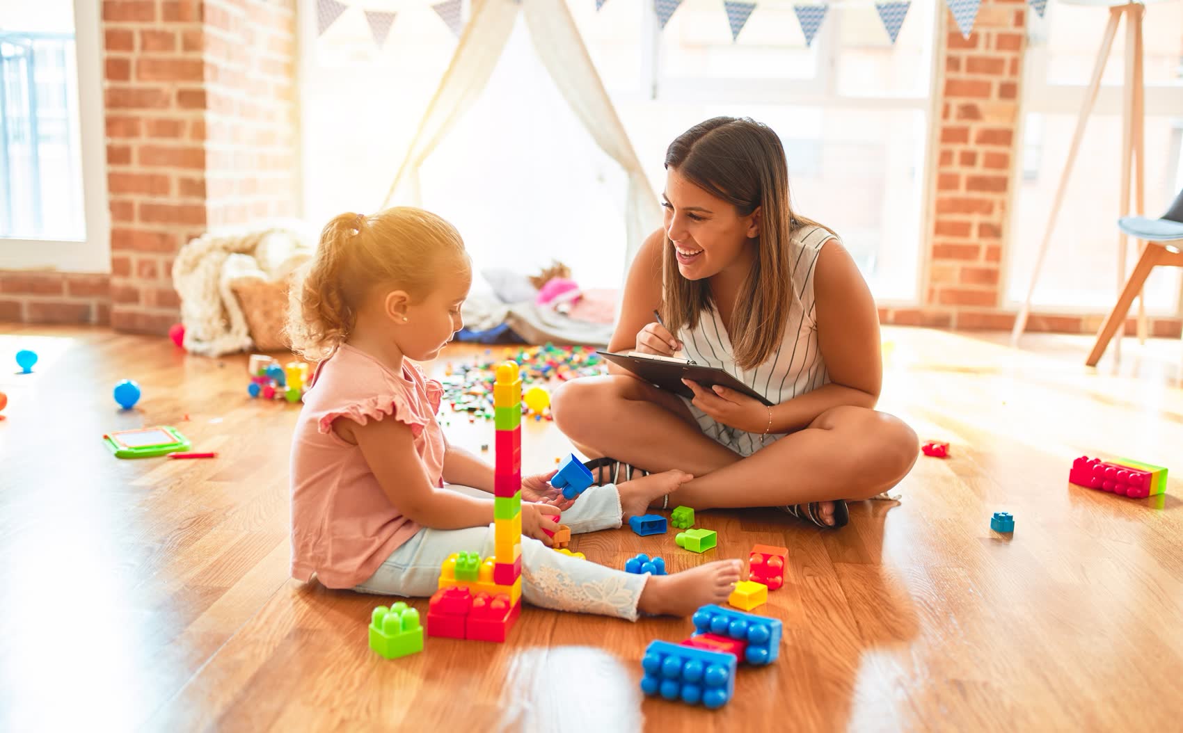 A therapist and a toddler building a block tower on a playroom floor