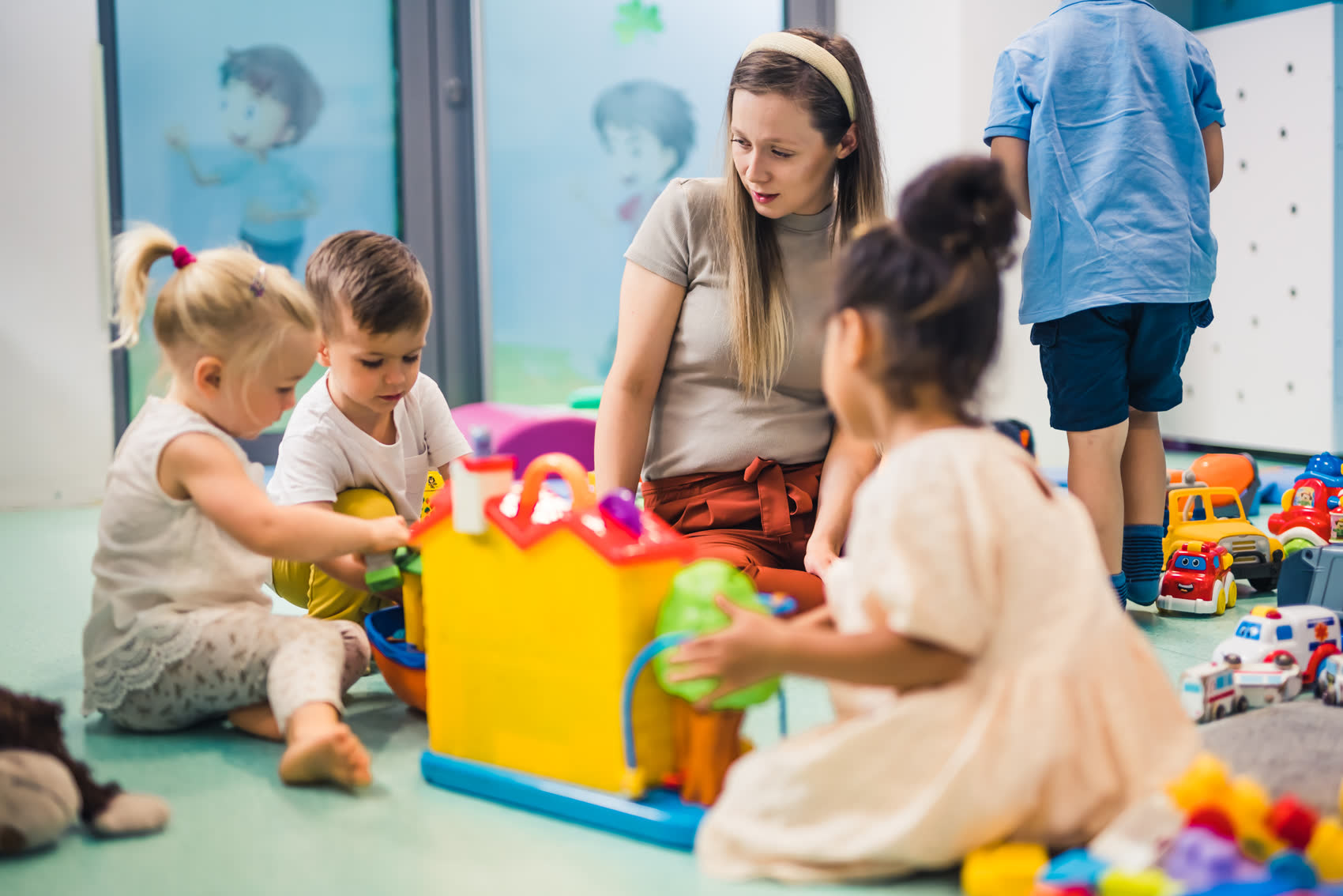 A teacher building with blocks alongside young children in a classroom full of toys