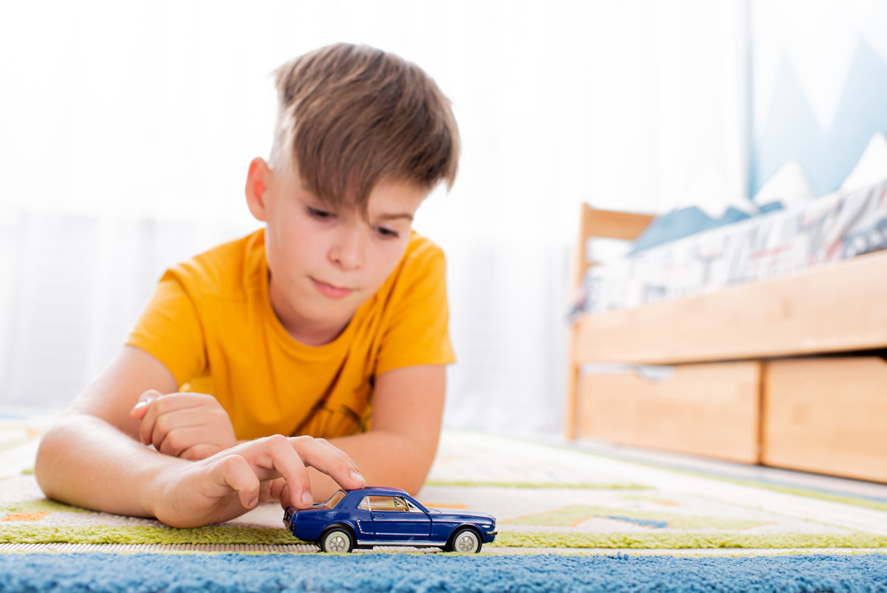 A young boy absorbed in a toy car on his own, eyes down