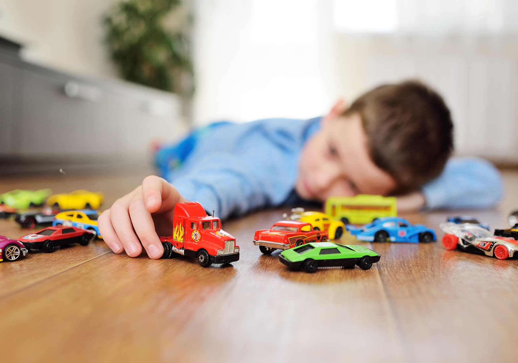 A young boy lying on the floor at eye level with a row of toy cars