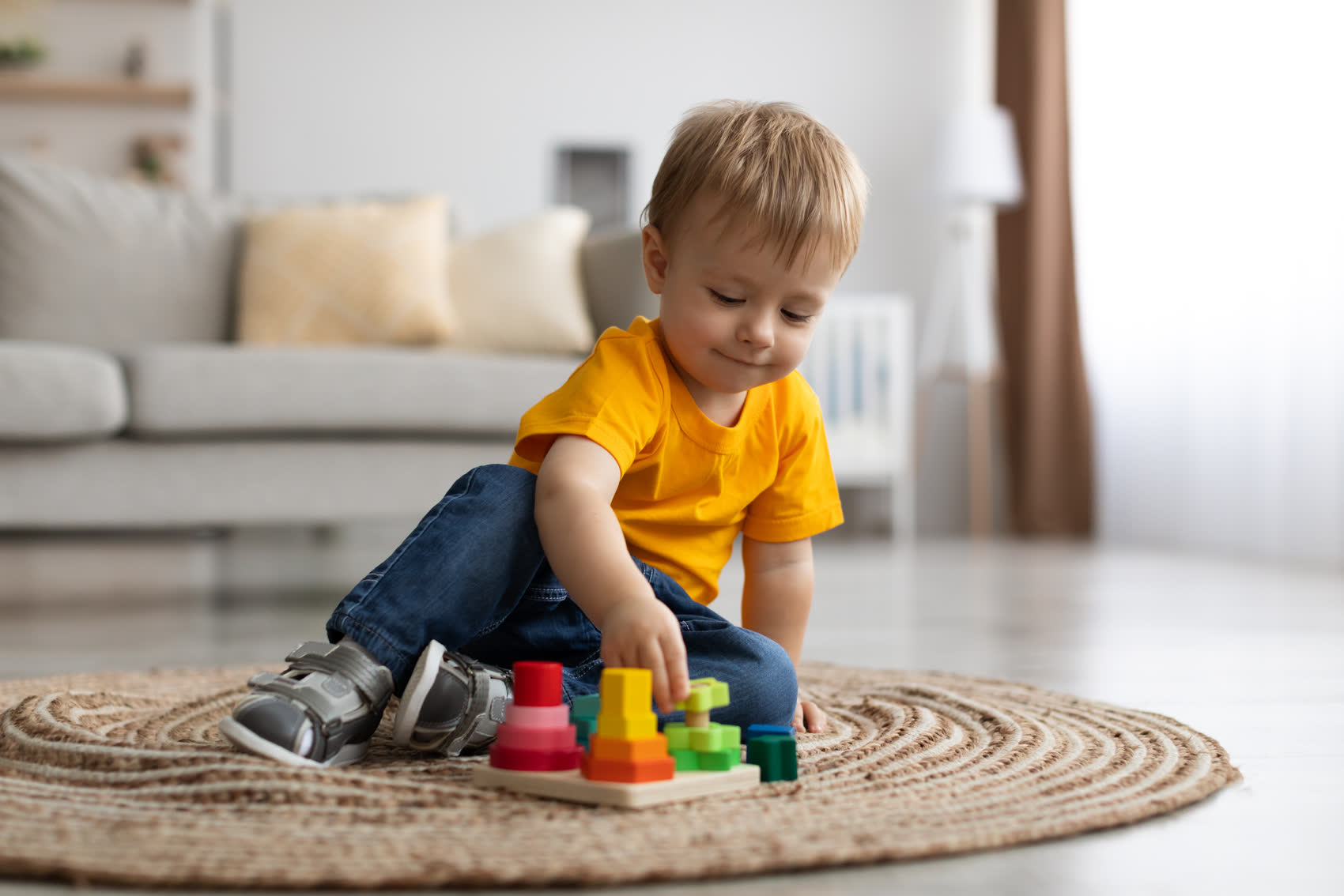 A toddler playing on his own with a wooden toy on the rug