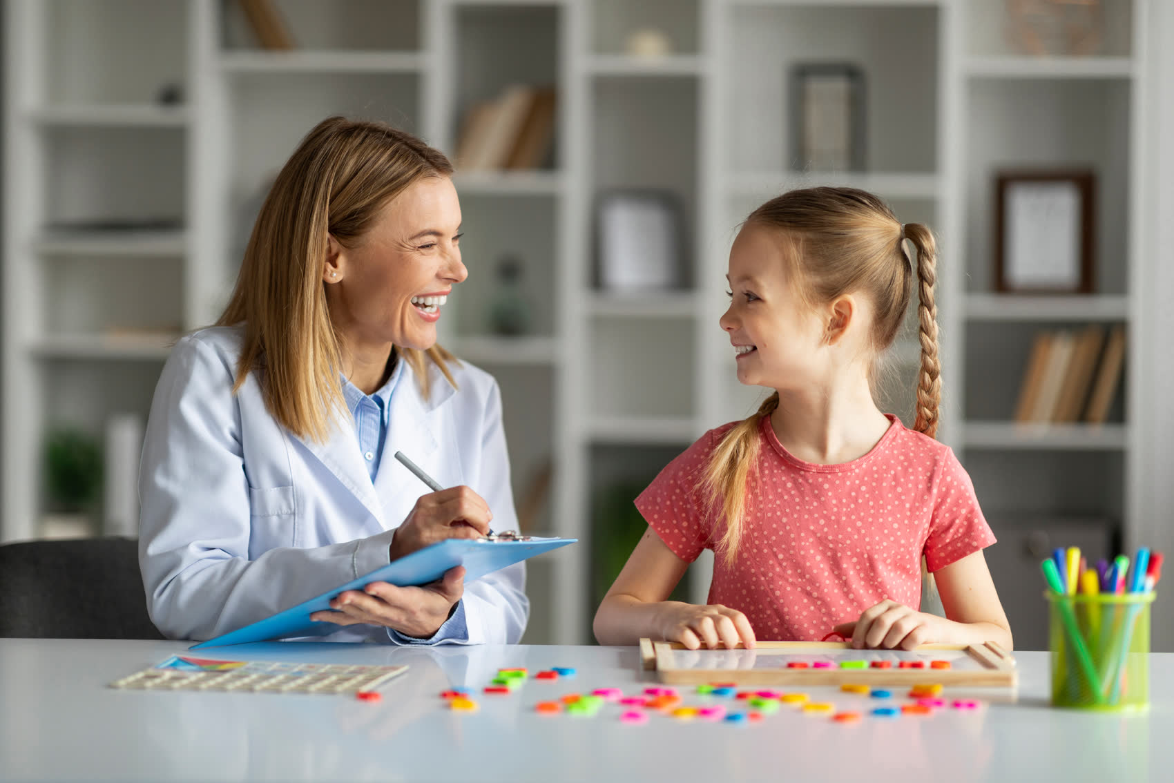 A child development specialist working with a smiling girl and taking notes